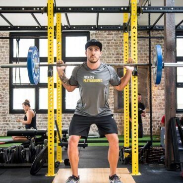 Fitness playground employee performing a back squat at a power rack